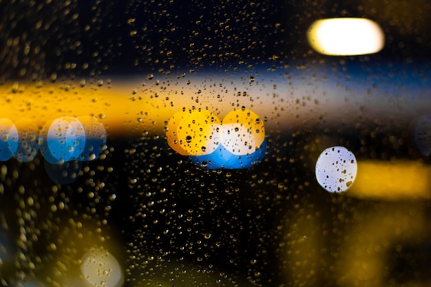 Goutte d'eau aux fenêtres et bokeh de la ville au coucher du soleil.