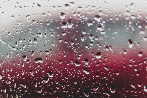 une goutte d'eau sur une fenêtre avec un fond rouge