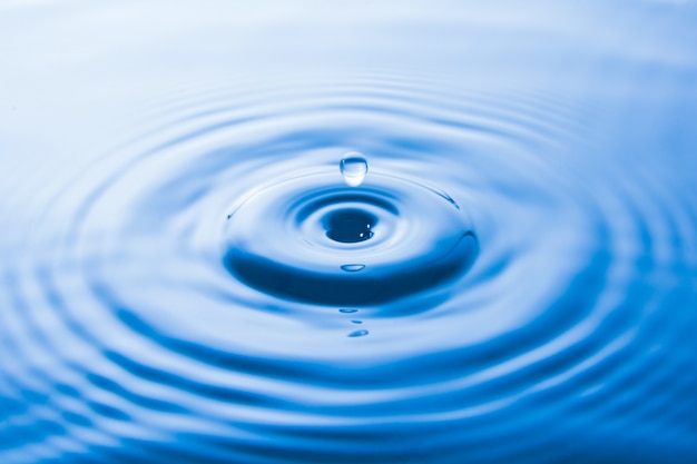 Photo la goutte d'eau tombant dans l'eau fait des vagues. éclaboussure d'eau ou fond de goutte d'eau.