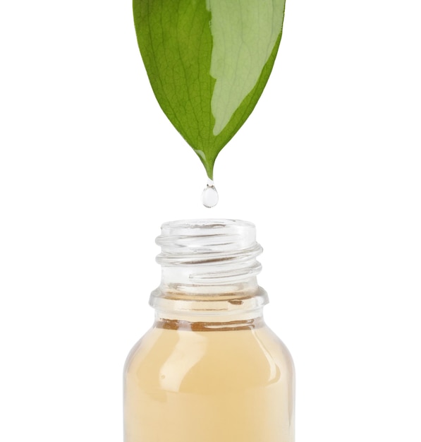 Goutte d'huile essentielle tombant de la feuille verte dans une bouteille en verre sur fond blanc gros plan