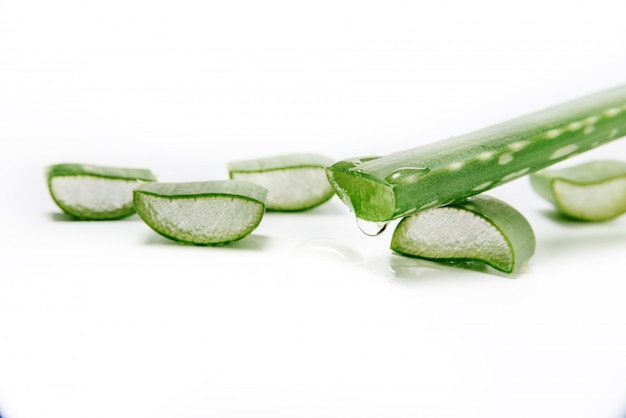 Une goutte de jus coule d'une tranche fraîche sur un gros plan de feuilles d'aloe vera.