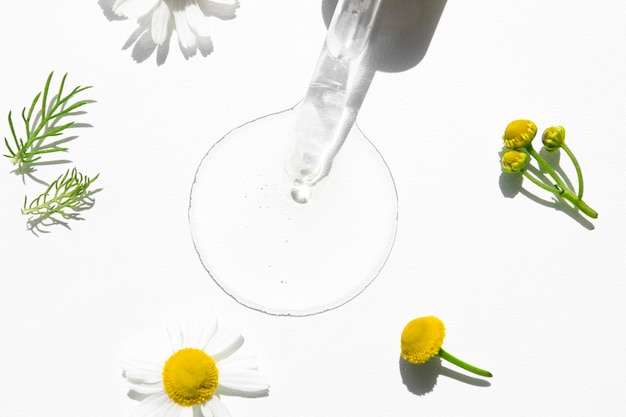 Goutte de liquide cosmétique transparente avec un compte-gouttes en verre sur fond blanc et camomille curative