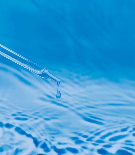 une goutte de liquide s'écoulant d'une pipette sur fond bleu