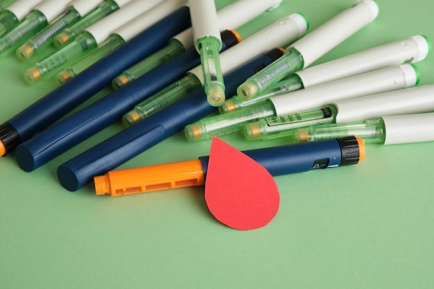 Une goutte de papier de sang et beaucoup de stylos à seringue avec de l'insuline sur un fond vert