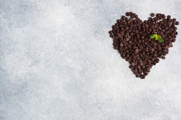 Gouttes de chocolat disposées en forme de cœur sur un béton gris. Morceaux de chocolat pour la décoration des desserts.
