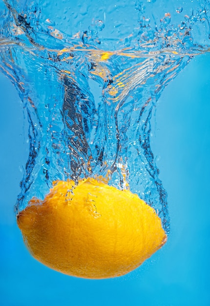 Gouttes de citron frais dans l'eau avec une touche sur un espace bleu