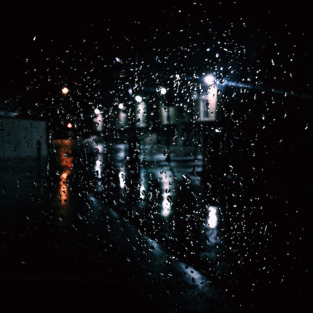 Photo des gouttes d'eau sur la fenêtre de la voiture dans la rue la nuit.