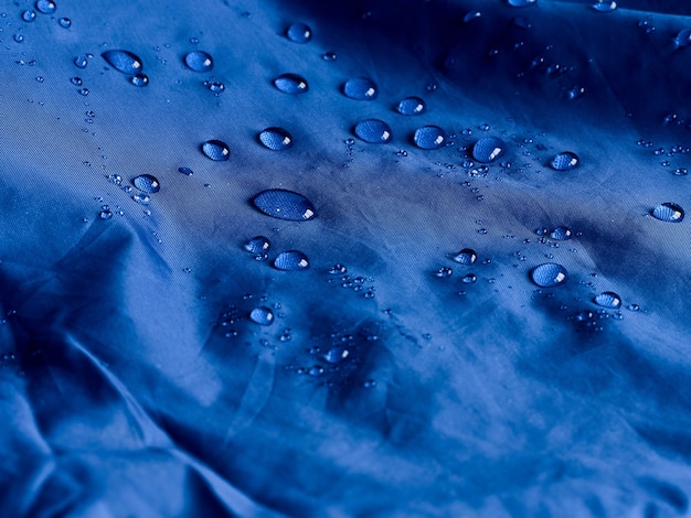 Gouttes d'eau sur le tissu de la membrane imperméable. Vue détaillée de la texture du tissu imperméable bleu.