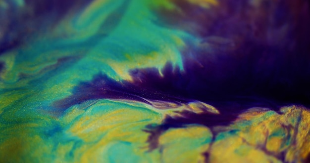 Des gouttes d'encre scintillante, un liquide brillant, défocalisé, de couleur violette, bleue et jaune, des particules de sable doré étincelantes.