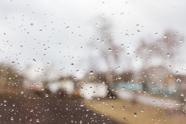 Gouttes de pluie sur du verre clair, loin des maisons floues et des arbres