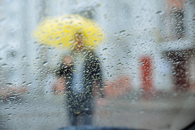 Gouttes de pluie humide sur verre homme avec silhouette jaune à travers le verre humide