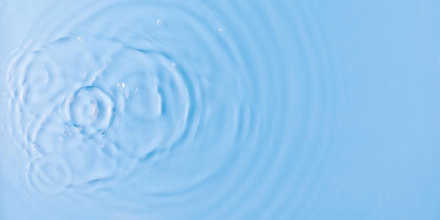 Les gouttes tombent dans l'eau douce claire sur fond bleu clair vue d'en haut