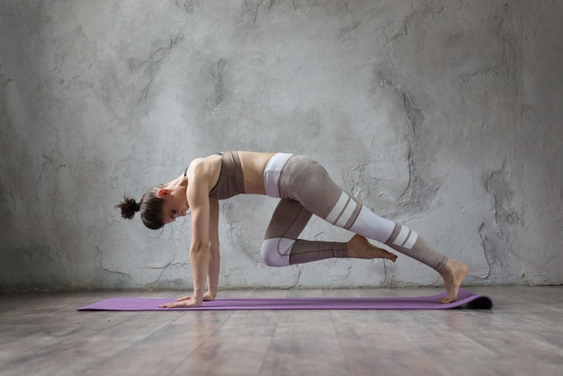 Gracieuse jeune femme brune faisant des étirements et des poses de yoga à la maison ou au studio de yoga