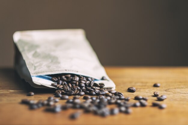 Photo grain de café sortant d'un sac en papier sur une table en bois