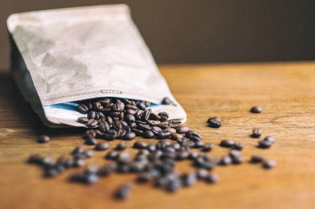 Grain de café sortant d'un sac en papier sur une table en bois