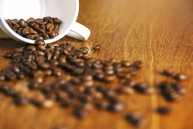 Grain de café sortant d'une tasse blanche sur une table en bois