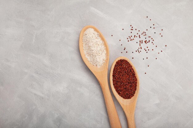 Grain de quinoa rouge et farine grossière Ragi dans des cuillères en bois sur fond gris texturé