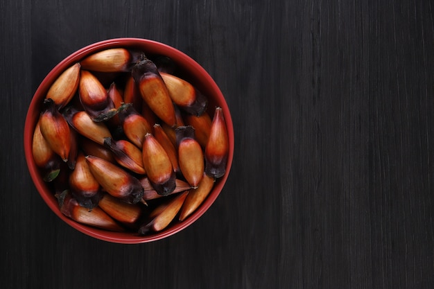 Graines d'araucaria typiques utilisées comme condiment dans la cuisine brésilienne en hiver. Pignons brésiliens dans un bol en bois marron et rouge sur fond de bois gris.