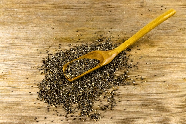 Photo graines de chia salvia hispanica dans une cuillère en bois sur une vieille table en bois naturel. concept d'aliments sains, de superaliments et de suppléments. fermer. mise au point sélective. copier l'espace