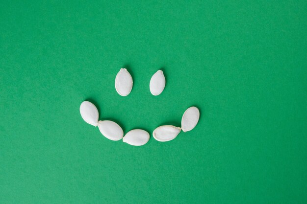 Les graines de citrouille non pelées sont disposées dans un smiley sur un espace de copie de fond vert