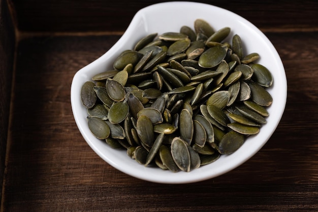 Graines de citrouille pelées dans une assiette sur un plateau en bois