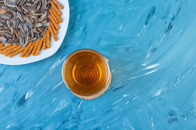 Graines et croûtons sur une assiette à côté d'une chope de bière, sur fond bleu.