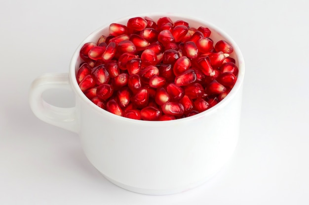 Graines de grenade dans une tasse blanche sur fond blanc. nourriture vitaminée