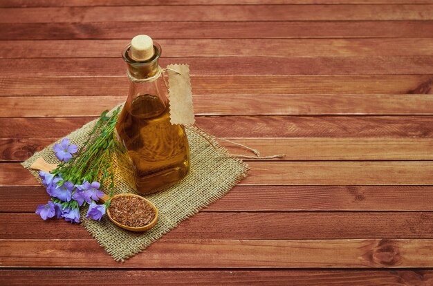 Graines de lin dans une cuillère en bois, plantes de lin avec fleur et huile de lin sur une bouteille en verre avec un sac vintage sur fond de bois. Photo conceptuelle pour la médecine et la nutrition diététique.