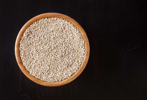 Graines de quinoa blanc séché dans un bol en bois sur fond de bois noir