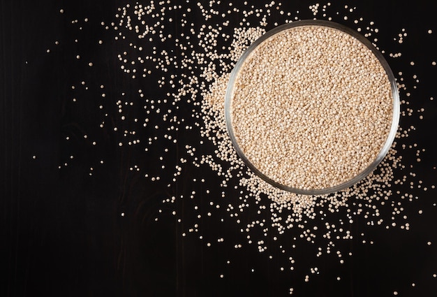 Graines de quinoa blanc séché sur fond de bois noir