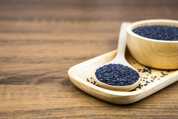 Graines de sésame noires dans une cuillère et une tasse en bois.