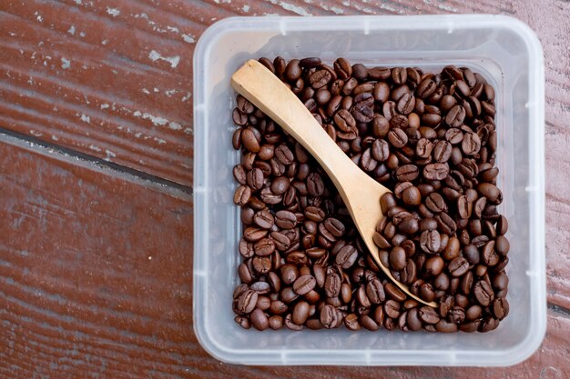 Grains de café, boîte en forme de carré avec une cuillère en bois. Surface en bois.