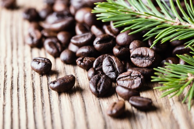 Grains de café avec une branche de sapin sur une surface en bois.