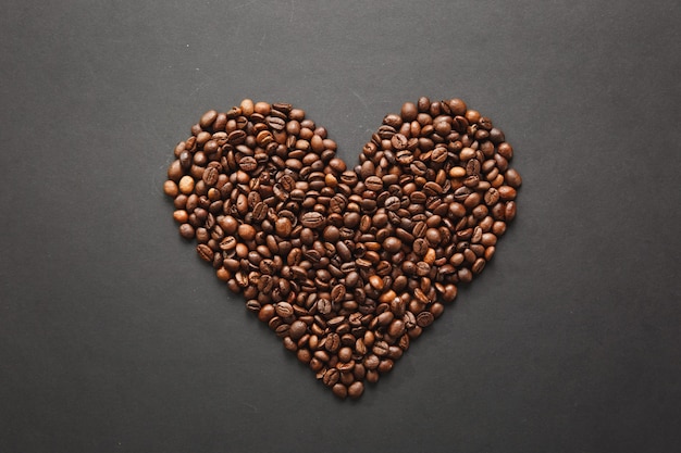 Grains de café bruns en forme de coeur isolés sur fond de texture noire pour la conception. Carte de Saint Valentin le 14 février, concept de vacances.