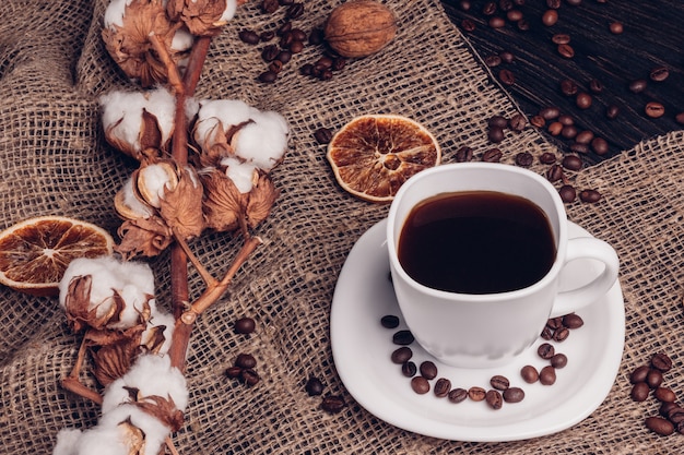 Grains de café à côté d'une tasse de café avec du coton sur le sac