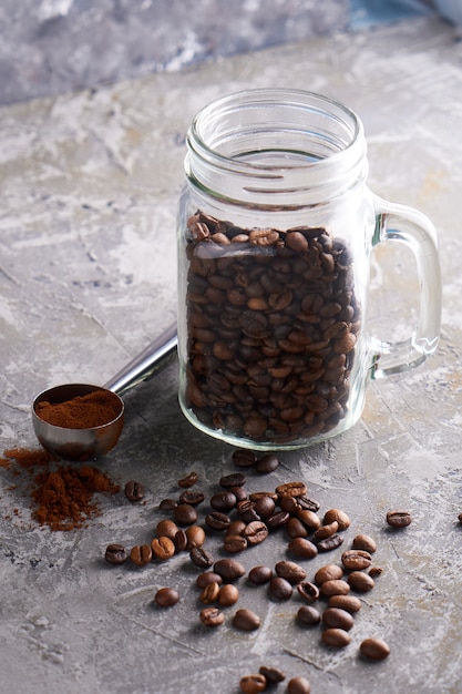 Grains de café dans un bocal en verre sur une table grise Copy space