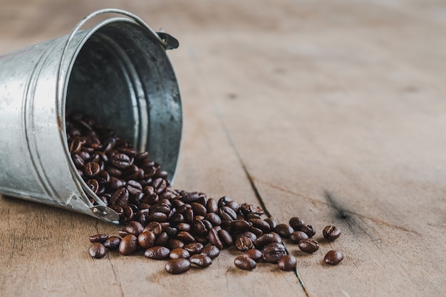 Grains de café dans un seau en métal sur plancher en bois