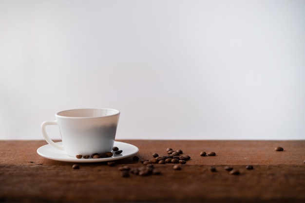 Les grains de café dans une tasse blanche est sur une table en bois brun foncé, avec un arrière-plan flou.