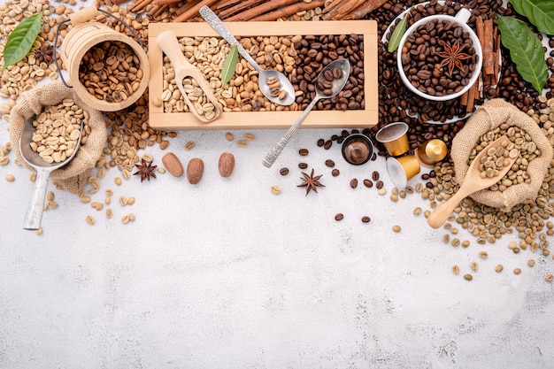 Grains de café décaféiné vert et brun non torréfiés et torréfiés foncés dans une boîte en bois avec des cuillères sur du béton blanc.