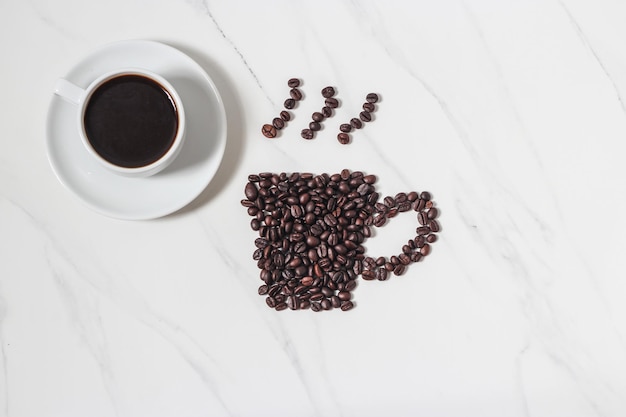 Grains de café épars et tasse à café expresso sur fond de marbre