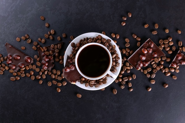 Grains de café épars, une tasse et du chocolat noir sur une table en pierre noire. Espace de copie.