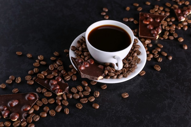 Grains de café épars, une tasse et du chocolat noir sur une table en pierre noire. Espace de copie.