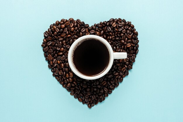 Grains de café en forme de coeur avec tasse blanche sur fond bleu