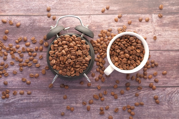 grains de café frais dans une tasse et réveil sur table