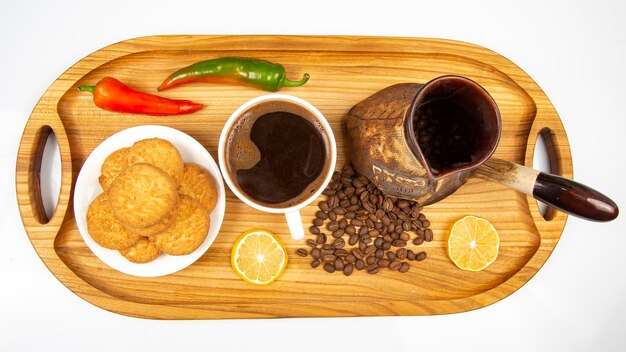 Les grains de café frais tombent des ustensiles de préparation du café en céramique cassés sur une planche de bois à côté du poivre et du citron