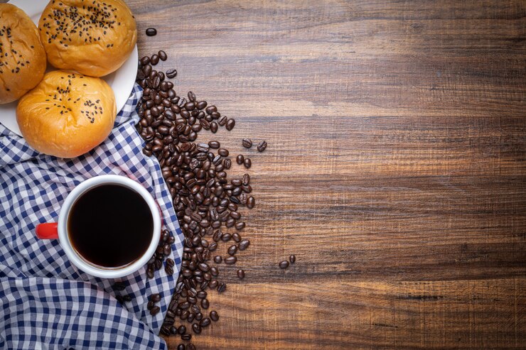 Photo grains de café noir et brun avec tasse de boisson chaude et pains sur table en bois, vue de dessus copie espace