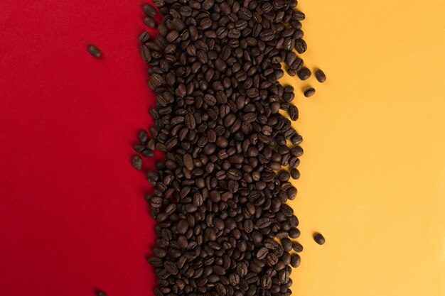 Les grains de café sont dispersés sur un gros plan de papier rouge et jaune, surface commerciale.