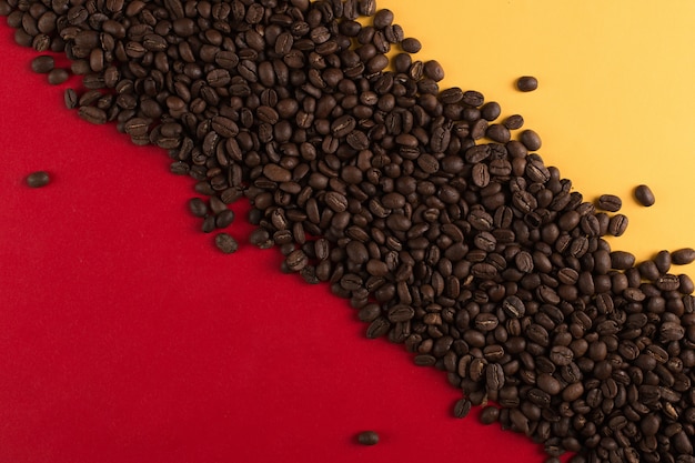 Les grains de café sont dispersés sur un gros plan de papier rouge et jaune, surface commerciale.