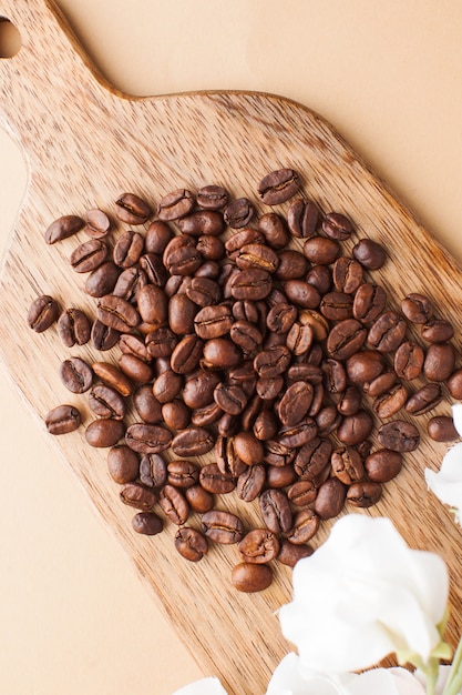 Les grains de café sont éparpillés sur une planche de bois sur un fond marron. Photo verticale.