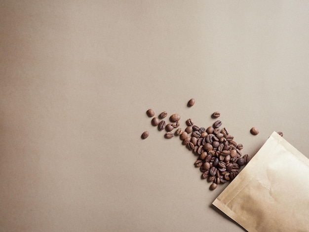 Grains de café sortant d'un sac en papier sur une vue de dessus de fond brun uni avec espace de copie